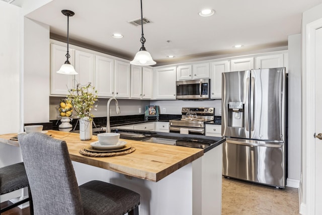 kitchen with visible vents, a peninsula, white cabinets, stainless steel appliances, and wood counters