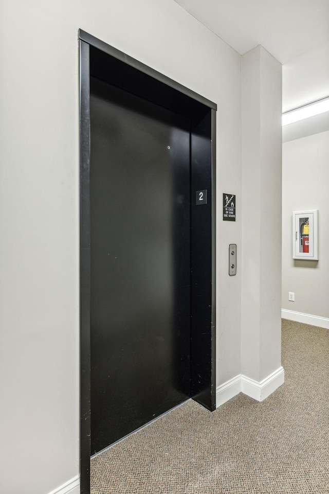 room details with baseboards, elevator, carpet floors, and a fire extinguisher