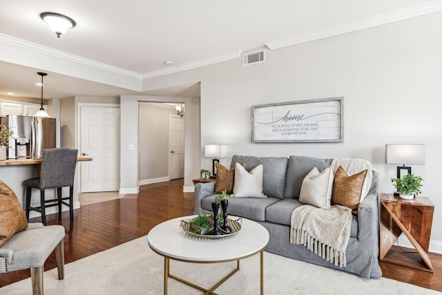 living room with visible vents, baseboards, ornamental molding, and light wood finished floors