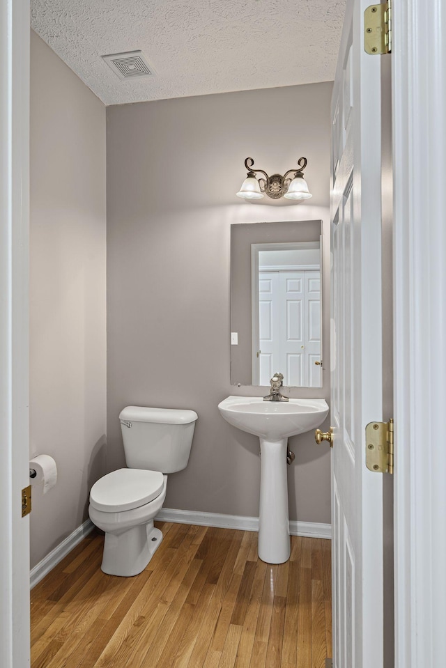 half bath featuring visible vents, baseboards, toilet, wood finished floors, and a textured ceiling