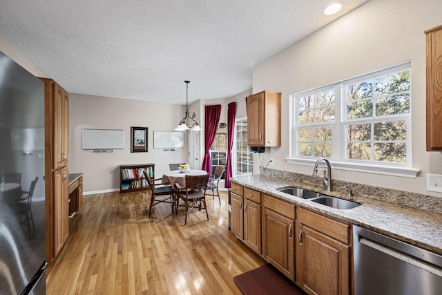 kitchen featuring light wood-style flooring, a sink, hanging light fixtures, appliances with stainless steel finishes, and brown cabinets