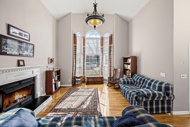 living room featuring a glass covered fireplace, vaulted ceiling, baseboards, and light wood finished floors