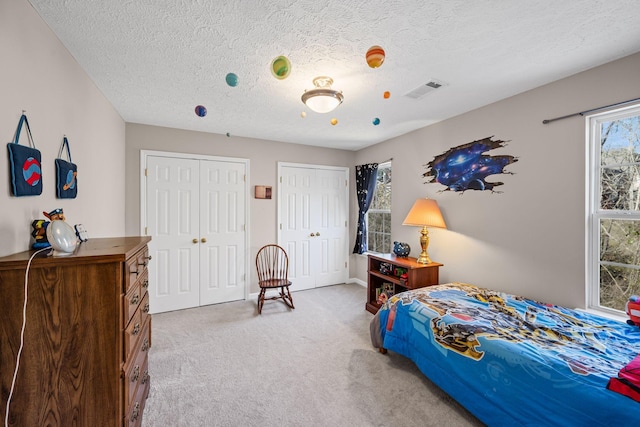 bedroom with visible vents, a textured ceiling, two closets, and carpet