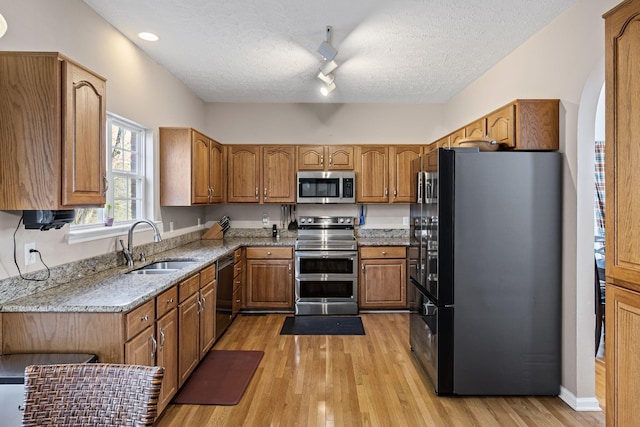 kitchen featuring black appliances, brown cabinetry, light wood-type flooring, and a sink