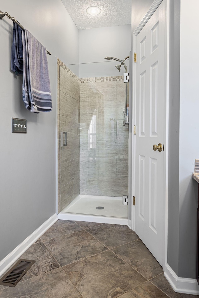 bathroom featuring a shower stall, baseboards, visible vents, and a textured ceiling