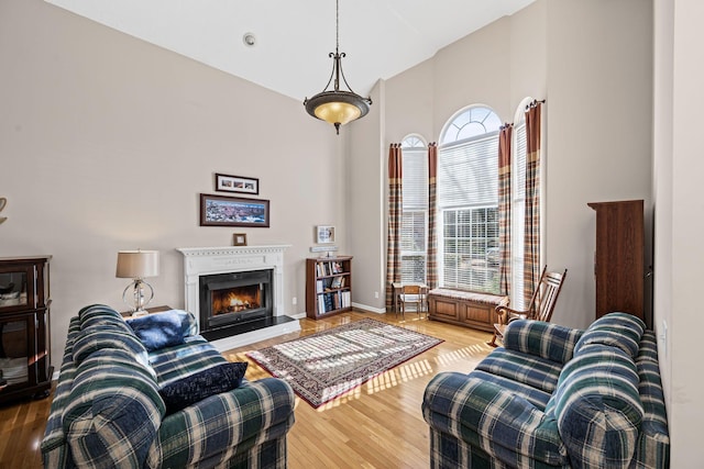 living area with baseboards, high vaulted ceiling, a warm lit fireplace, and light wood finished floors