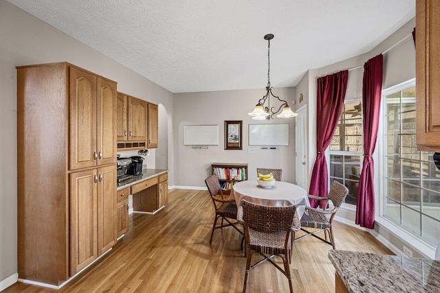 dining space featuring baseboards, light wood-style floors, arched walkways, and a textured ceiling