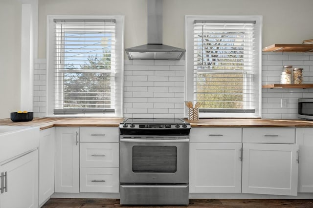 kitchen featuring open shelves, wood counters, stainless steel electric stove, white cabinets, and wall chimney range hood