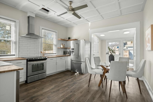 kitchen with wood counters, decorative backsplash, appliances with stainless steel finishes, wall chimney exhaust hood, and dark wood-style flooring