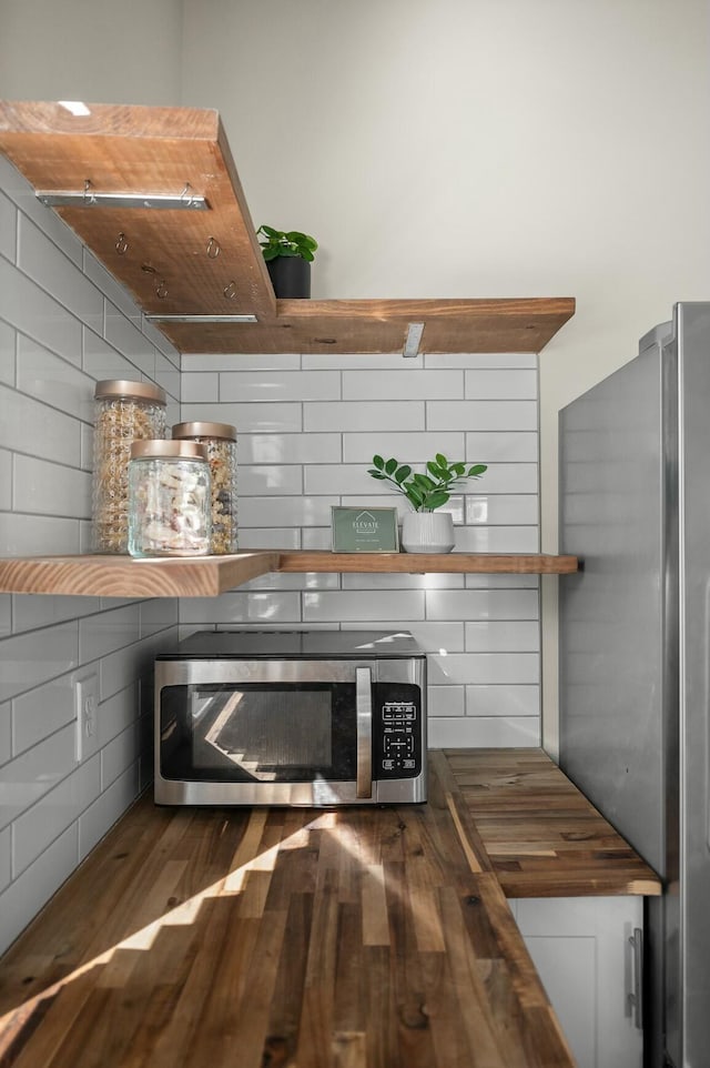 room details with open shelves, backsplash, wooden counters, and stainless steel appliances