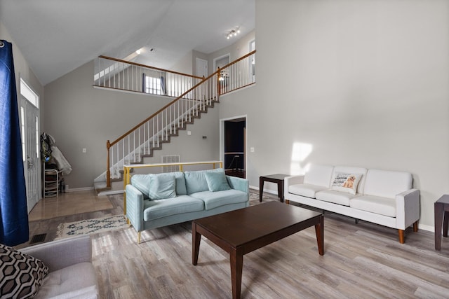 living room featuring stairway, baseboards, high vaulted ceiling, and wood finished floors