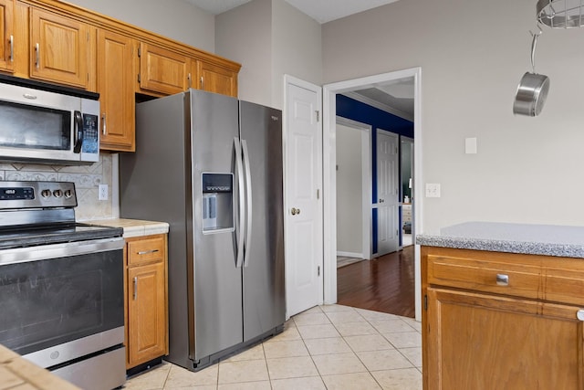 kitchen featuring light tile patterned floors, decorative backsplash, brown cabinets, and appliances with stainless steel finishes