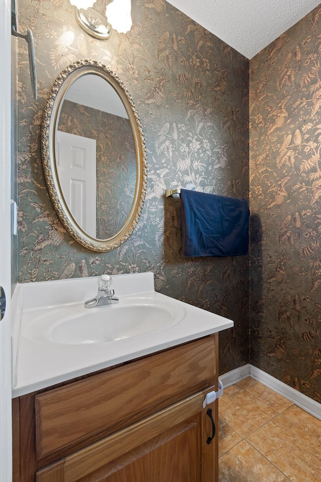 bathroom featuring wallpapered walls, a textured ceiling, tile patterned flooring, baseboards, and vanity