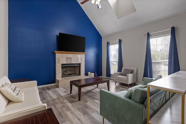 living room featuring high vaulted ceiling, wood finished floors, a ceiling fan, and a tile fireplace