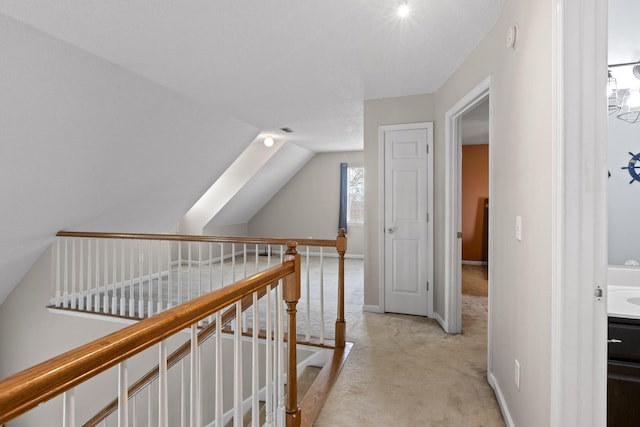 hall with vaulted ceiling, an upstairs landing, light colored carpet, and baseboards