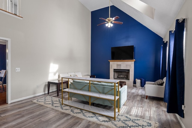 living area with baseboards, wood finished floors, a tile fireplace, and high vaulted ceiling