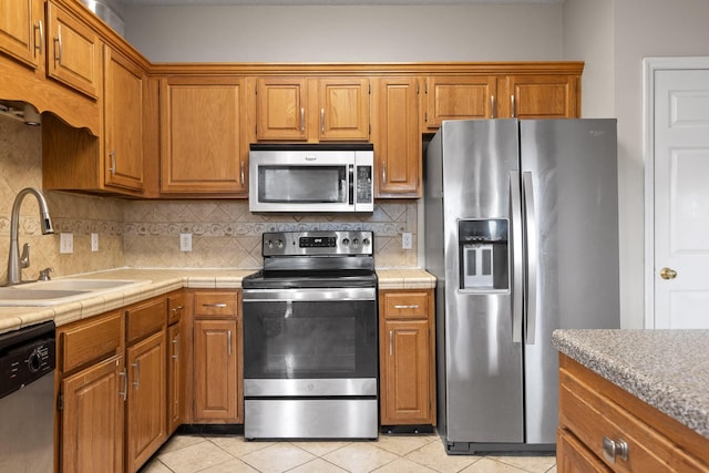 kitchen with light tile patterned floors, decorative backsplash, brown cabinets, stainless steel appliances, and a sink