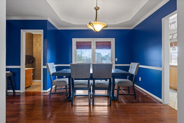 dining area featuring hardwood / wood-style floors, a tray ceiling, and baseboards