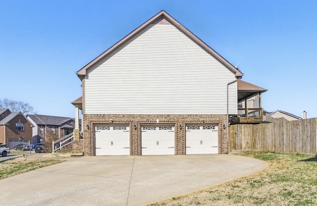 view of side of home with brick siding, driveway, a garage, and fence