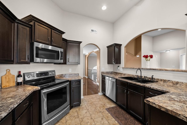 kitchen with visible vents, a sink, stainless steel appliances, arched walkways, and dark brown cabinets