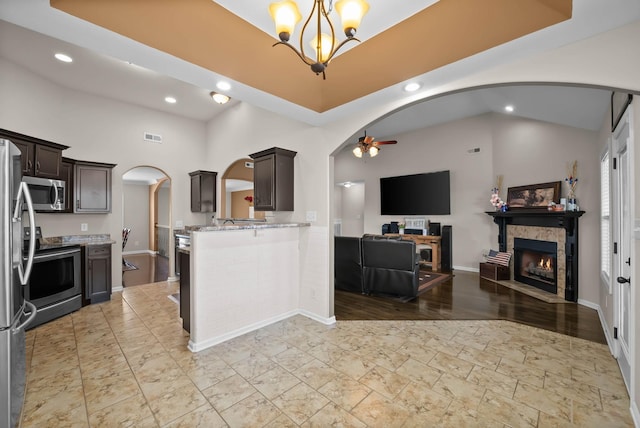 kitchen featuring ceiling fan with notable chandelier, open floor plan, arched walkways, appliances with stainless steel finishes, and light stone countertops