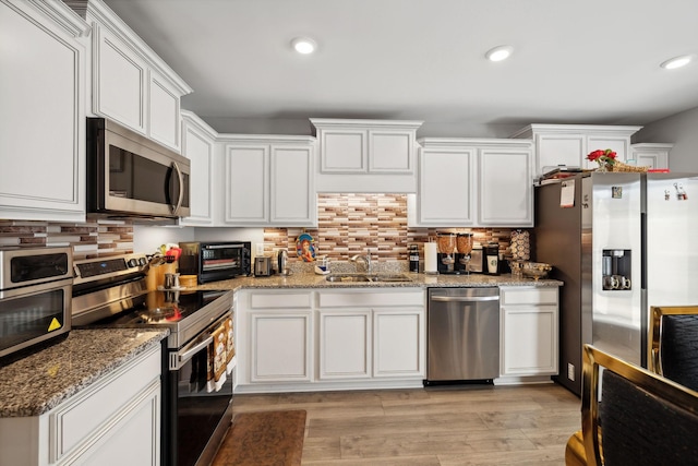 kitchen featuring a sink, decorative backsplash, stainless steel appliances, white cabinets, and light wood-style floors