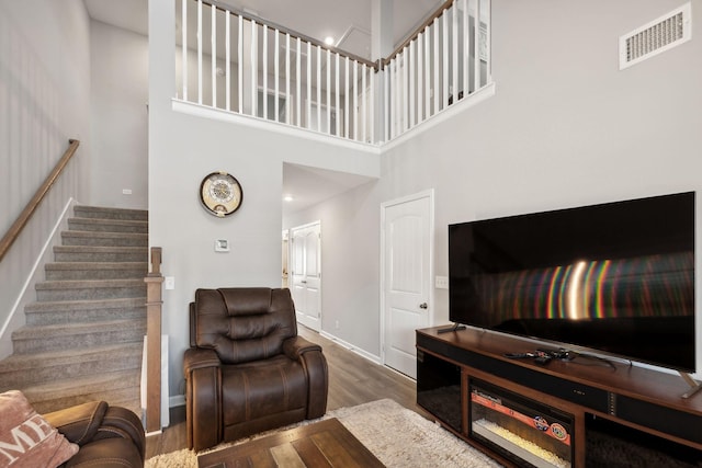 living area featuring visible vents, baseboards, stairway, a high ceiling, and wood finished floors