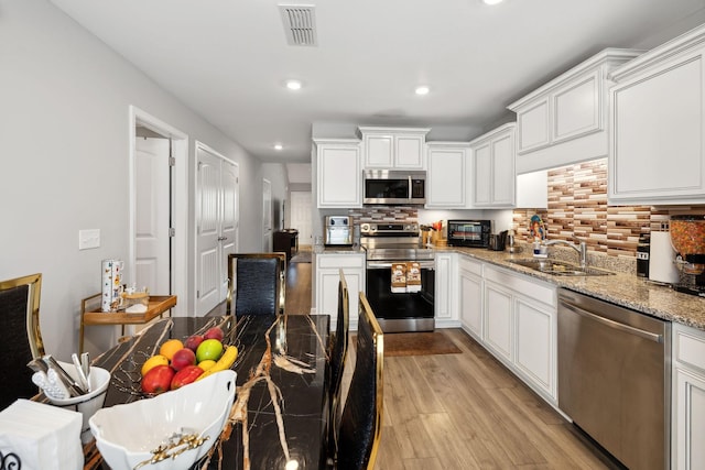 kitchen with visible vents, decorative backsplash, light wood-style flooring, stainless steel appliances, and a sink