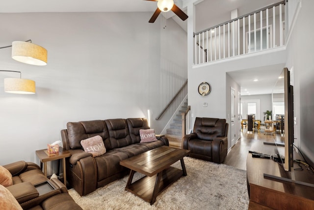 living area with stairway, high vaulted ceiling, a ceiling fan, and wood finished floors