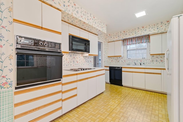 kitchen with wallpapered walls, light countertops, white cabinets, black appliances, and a sink