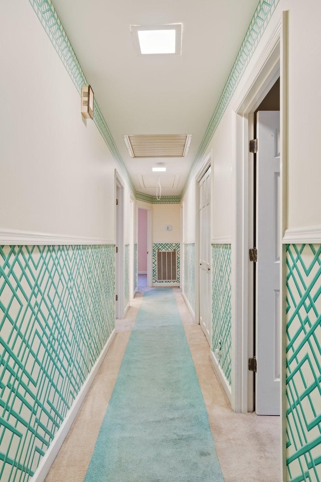 corridor with visible vents, a wainscoted wall, wallpapered walls, light colored carpet, and attic access