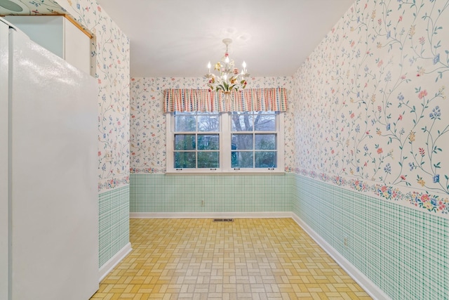 empty room with wallpapered walls, visible vents, a chandelier, and wainscoting