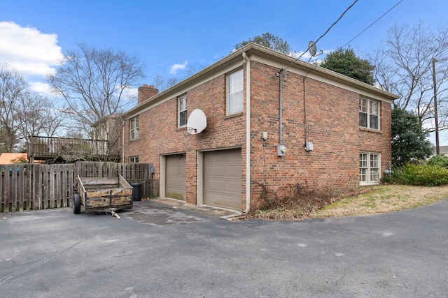 view of home's exterior featuring brick siding, fence, aphalt driveway, a chimney, and a garage