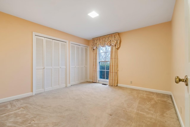 unfurnished bedroom featuring carpet, multiple closets, and baseboards