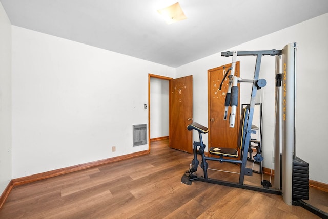 workout area with heating unit, wood finished floors, and baseboards