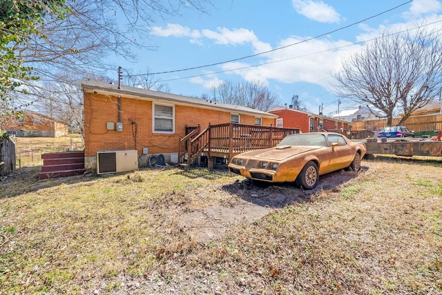 rear view of property featuring a wooden deck, brick siding, central AC unit, and fence