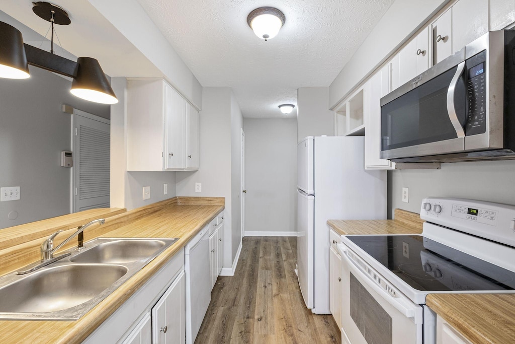 kitchen featuring white appliances, a sink, a textured ceiling, white cabinetry, and light wood-type flooring