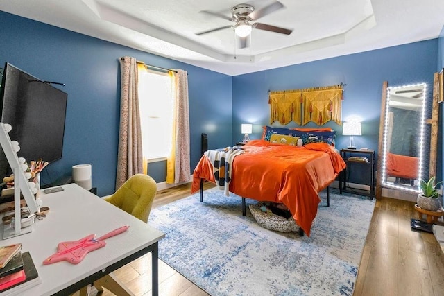 bedroom with ceiling fan, a tray ceiling, and wood finished floors