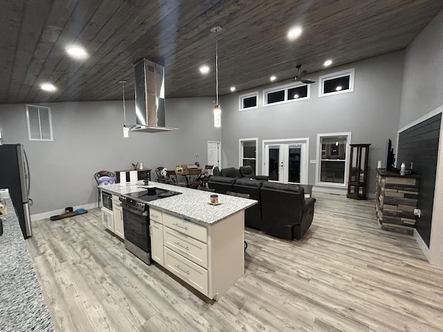 kitchen with a center island with sink, light wood-style flooring, appliances with stainless steel finishes, white cabinets, and extractor fan