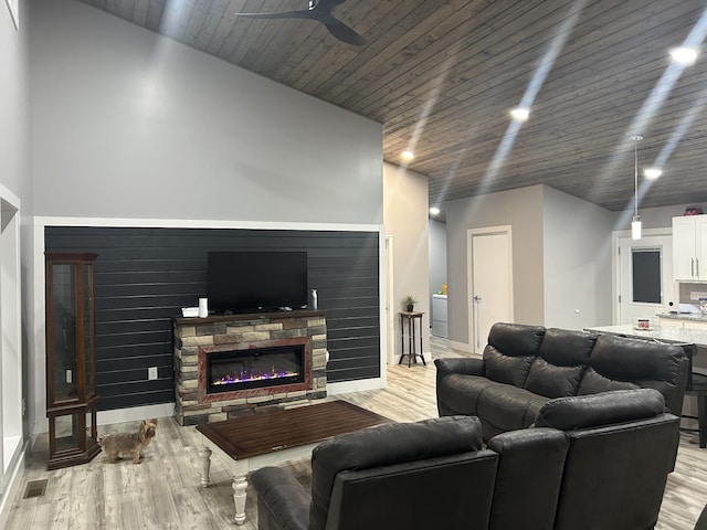 living room with a stone fireplace, wood ceiling, light wood finished floors, and a ceiling fan