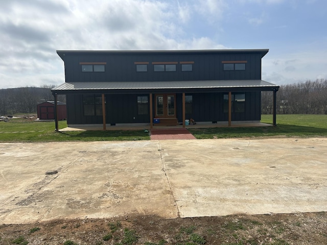 modern inspired farmhouse featuring a front yard, covered porch, a storage unit, french doors, and board and batten siding