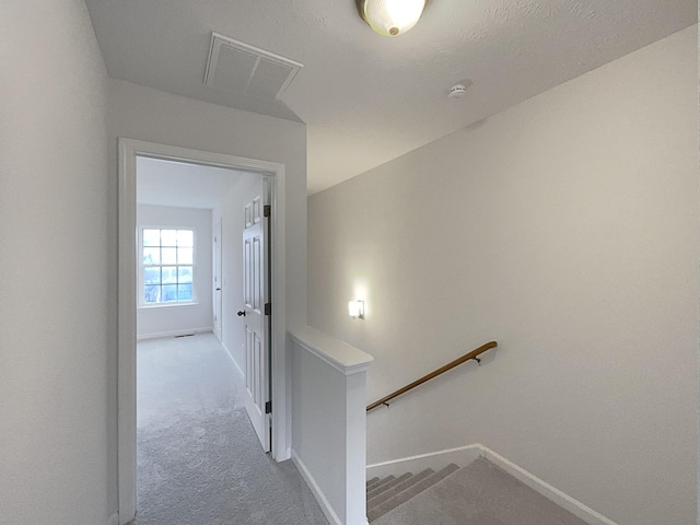 hall with an upstairs landing, carpet, visible vents, and baseboards