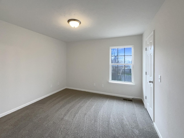 spare room featuring visible vents, baseboards, and dark carpet