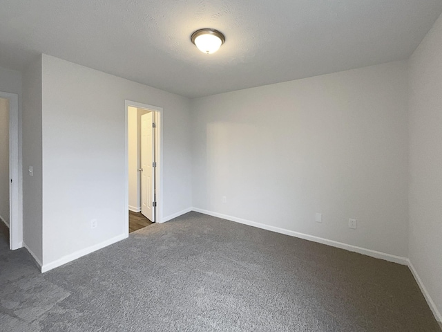 unfurnished room featuring dark carpet and baseboards