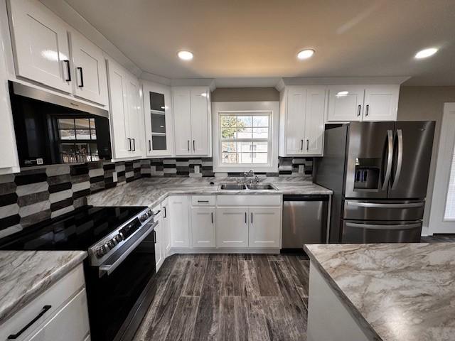 kitchen with backsplash, light stone countertops, appliances with stainless steel finishes, white cabinets, and a sink