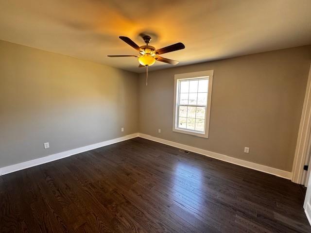 empty room featuring visible vents, ceiling fan, baseboards, and dark wood-style flooring