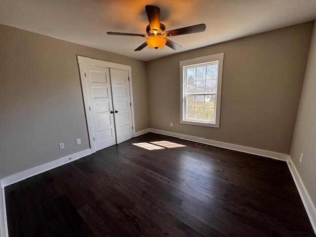 unfurnished bedroom with ceiling fan, a closet, baseboards, and dark wood-style floors