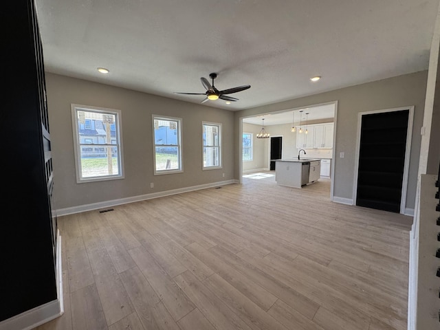 unfurnished living room with visible vents, baseboards, light wood-type flooring, ceiling fan with notable chandelier, and a sink