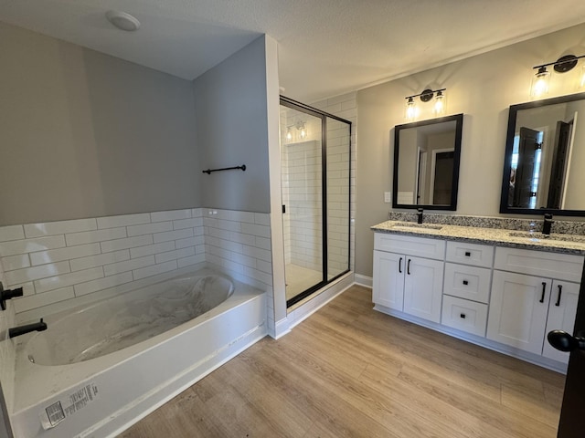 bathroom featuring a bath, a stall shower, wood finished floors, and a sink