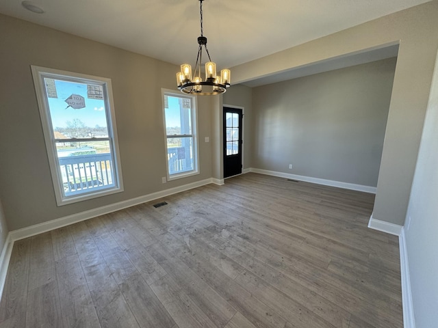 empty room featuring a notable chandelier, visible vents, baseboards, and wood finished floors